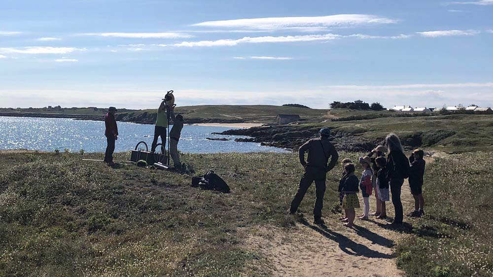 Researchers standing in a coastal landscape talking to a group of school children 